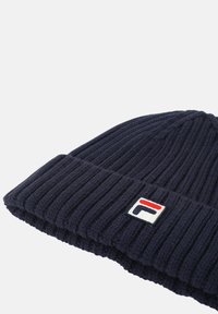 Beanie a coste di colore blu navy realizzato in tessuto testurizzato con risvolto, dotato di una piccola patch del logo in rosso, bianco e blu sul lato.