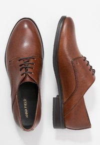 Chaussures de ville en cuir marron avec une finition lisse, à lacets, à bout rond et à talon bas. Présente des détails de couture subtils sur les côtés.
