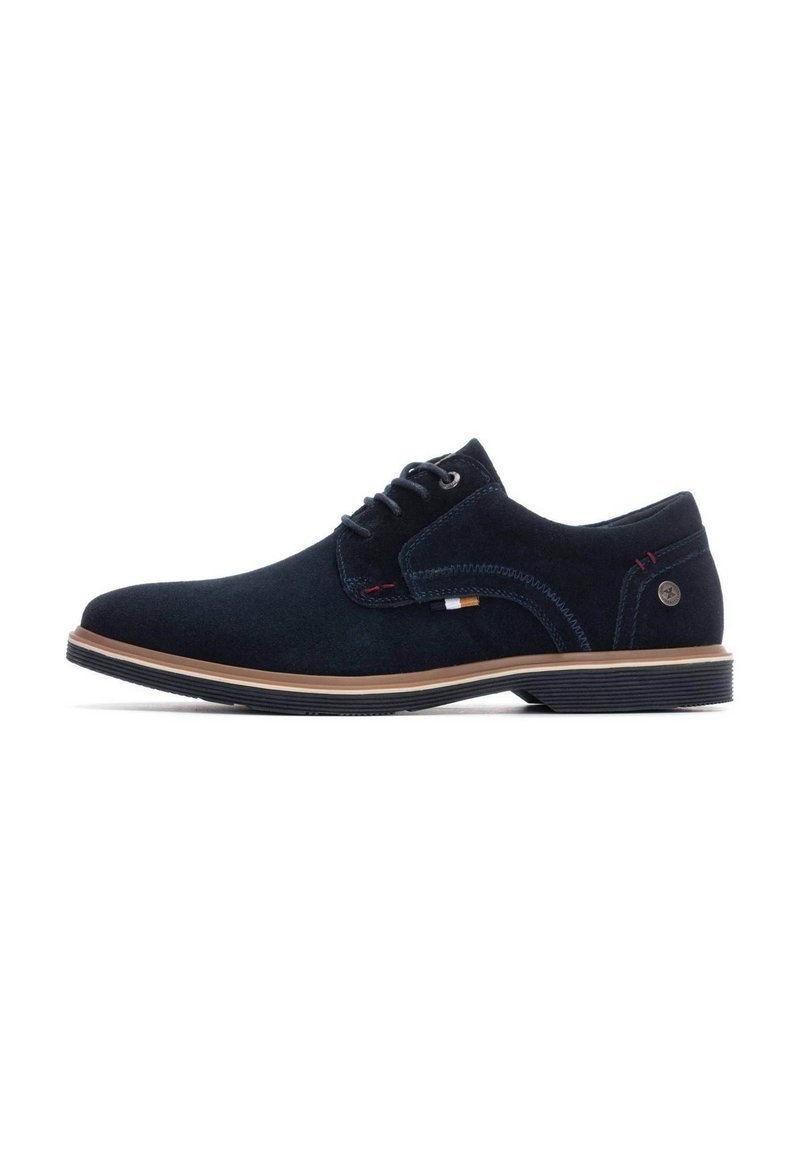 Zapatos de ante azul marino con cordones y una suela de color marrón claro contrastante, con detalles de costura y un pequeño logo en el lateral.