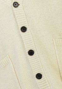 Krämfärgad stickad cardigan med V-ringning, fem svarta knappar, ribbat mönster och en framficka.