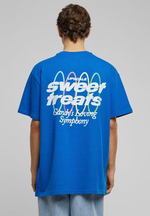 Blå bomulds t-shirt med stort hvidt tekst på ryggen, der står "sweet treats" med farverige cirkulære accenter og mærkenavn ovenfor.