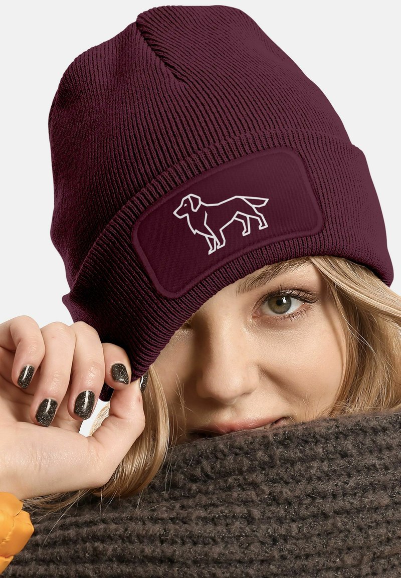 Burgundy knit beanie with a white outline of a dog on a rectangular patch. Features ribbed texture and snug fit.