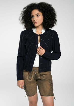 Marine gebreide cardigan met diamanten patronen, ronde halslijn en knoopsluiting. Gestyleerd met beige geborduurde shorts.