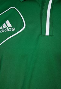 Polo vert en tissu respirant, avec un logo Adidas blanc et un passepoil blanc contrastant le long du col et des coutures d'épaules.