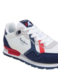 Meeste sneaker valge nahk ülaosaga, tumesiniste sametdetailide, punaste ja siniste triipudega ning kummist tallaga. Omab pehmendatud krae ja logodetaili.