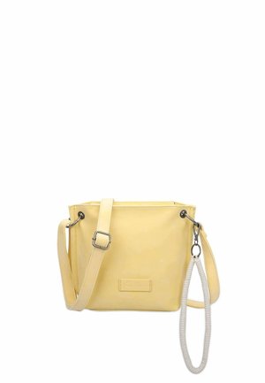 Mała bladożółta torebka na ramię z regulowanym paskiem, srebrnymi elementami i przymocowanym białym spiralnym brelokiem, na białym tle.