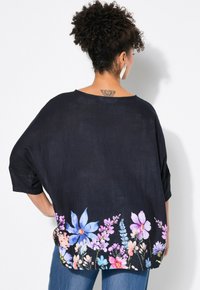 Luftiges schwarzes Oberteil aus leichtem Stoff, mit einem Blumenmuster in Blau- und Rosatönen am Saum und weiten Ärmeln.