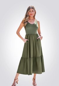 Olijfgroen mouwloze maxi-jurk met textuur op het lijfje, een gelaagde rok en zijzakken. Gestyled met sandalen met bandjes.