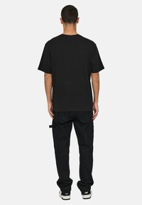 Black short-sleeve t-shirt with a relaxed fit, plain design, crew neck, paired with black cargo pants, textured fabric, and subtle pocket details.