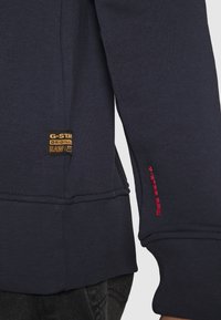 Felpa blu navy con tessuto strutturato, patch con il logo G-Star in oro e dettaglio di cuciture rosse sulla manica.