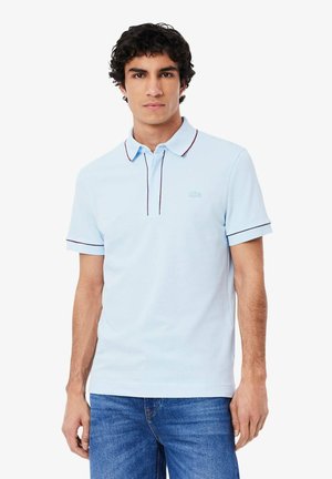 Polo shirt azzurro chiaro con colletto, dotato di una chiusura a due bottoni, rifiniture rosse e blu navy e un piccolo logo ricamato sul petto.