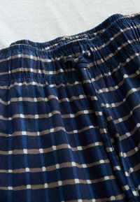 Pantalon à taille élastique avec un motif à carreaux bleu, gris et blanc, doté d'un cordon de serrage en tissu assorti noué.