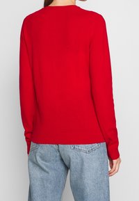 Roter Strickpullover mit langen Ärmeln und rundem Halsausschnitt. Verfügt über einen gerippten Saum und Bündchen und wird mit lässig sitzenden blauen Jeans präsentiert.