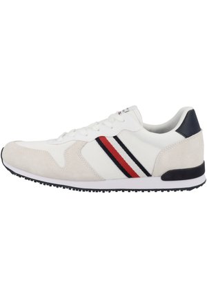 Witte lage sneaker met rode en zwarte zijstrepen, beige suède accenten, zwarte hielstrook en zwarte rubberen zool.
