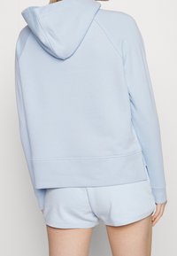 Jasnoniebieska bluza z kapturem o luźnym kroju i ściągaczem u dołu. Zestawiona z pasującymi jasnoniebieskimi szortami. Gładka faktura.