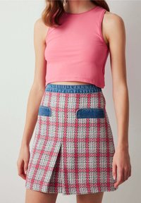 Top corto rosa con diseño ajustado combinado con una falda a cuadros que presenta patrones en rosa, verde y blanco, y detalles de mezclilla en los bolsillos.