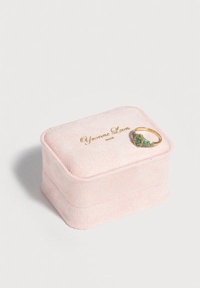 Μαλακό ροζ βελούδινο κουτί κοσμημάτων με χρυσό λογότυπο "Yvonne Lou", καλυμμένο με ένα χρυσό δαχτυλίδι με πράσινο πετράδι σε σχήμα σταγόνας και πλευρικές διακοσμήσεις.