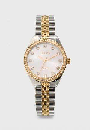 Silver and gold wristwatch with crystal hour markers, crystal-studded bezel, and white dial showing time at 10:09:31, metallic link band.