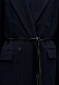 Marineblauwe wollen jas met een dubbelzijdig ontwerp, zwarte knopen en een zwart gestrikt ceintuur. Gelaagd stof met zijzakken.