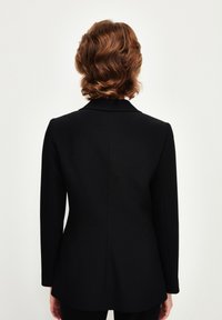 Černý sako s přiléhavým střihem, strukturovanými ramenními vycpávkami a dlouhými rukávy. Hladká tkanina s matným povrchem. Zobrazeno zádní pohled.