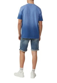 Blauwe gradiënt T-shirt met korte mouwen, gemaakt van katoen, gecombineerd met opgerolde denim shorts. Draagt witte sneakers en gestreepte sokken.