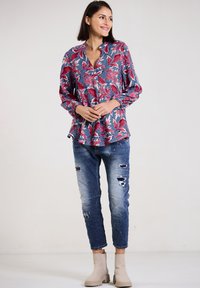 Floral blouse in blue, red, and white with long sleeves; paired with distressed blue jeans and beige ankle boots.
