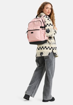 Pink backpack with black accents, featuring multiple compartments and zippers, made of durable fabric. Worn over gray clothing.