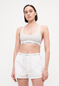Calvin Klein sportmelltartó világosszürkében, ismétlődő logó mintával, fehér sorttal párosítva, ami logós derékrésszel rendelkezik.