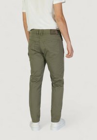 Pantalones slim-fit color caqui con bolsillos traseros, trabillas para cinturón y parche de la marca. Combinados con una camiseta blanca y zapatillas blancas. Material de algodón suave.