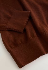 Rudas megztinis, pasižymintis lygiu paviršiumi, raukšlėtomis apykaklėmis ir hemu. Audinys turi minkštą, lengvą išvaizdą ir yra laisvas.