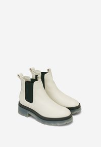 Botas Chelsea de cuero blanco con paneles laterales elásticos negros, tiradores y una suela transparente gruesa. Textura suave y diseño elegante.