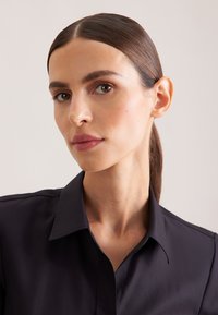 Czarna koszula z kołnierzykiem o gładkiej fakturze, z klasycznym fasonem i subtelnymi detalami szwów. Twarz częściowo widoczna.