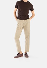 T-shirt marrone a maniche corte abbinata a pantaloni beige su misura e scarpe in pelle marrone scuro, con design alla corda e texture liscia.
