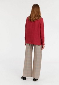 Chemise en lin rouge à coupe droite, avec couture au dos et poignets boutonnés. Associée à un pantalon à carreaux beige ample et des chaussures noires.