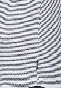 Černobílá pruhovaná látka s malými, rovnoměrně rozmístěnými tečkami. Obsahuje šev a štítek s nápisem "EST. 1993" blízko spodní části.