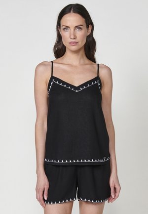 Set di top senza maniche neri e pantaloni corti con bordi ricamati bianchi. Tessuto morbido, design a scollo a V, vestibilità rilassata e dettagli decorativi coordinati.
