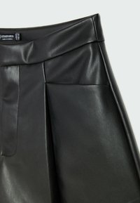 Černá kožená sukně má hladkou texturu, plisovaný design a dvě boční kapsy. Pas je strukturovaný, což zvýrazňuje celkovou siluetu.