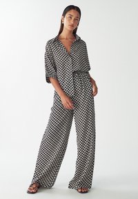 Black and white patterned jumpsuit with a collared neckline, short sleeves, and wide-leg design. Made of smooth, lightweight fabric.