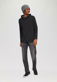 Schwarzes Langarm-Hoodie, graue Strickmütze, graue Jeans und schwarze Sneakers mit weißen Sohlen. Glatte Textur, minimalistisches Design.