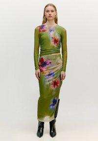 Langes, grünes Blumenkleid mit langen Ärmeln; weist Blumenmuster in Blau, Rot und Lila auf; schlanker Schnitt; kombiniert mit schwarzen kniehohen Stiefeln.