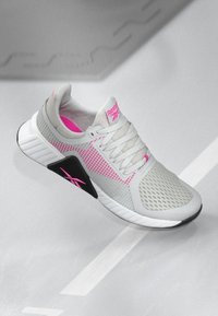 Gai pelēki un rozā Reebok sporta apavi ar sieta augšdaļu, baltu zoli, melnu sānu paneli un šņorēm, attēloti slīpi uz gaišas virsmas.