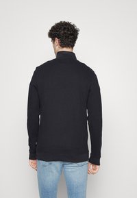 Zwarte lange mouw sweatshirt met een hoge kraag, gestructureerde stof en ribbenmanchetten, gecombineerd met lichtblauwe jeans. Minimalistisch ontwerp.