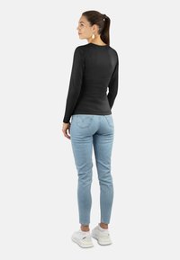 Schwarzes Langarmoberteil, körperbetontes Design. Hellblaue Jeans mit klassischem Schnitt. Weiße Sneaker mit dezenten Akzenten. Model steht mit dem Rücken zur Kamera.