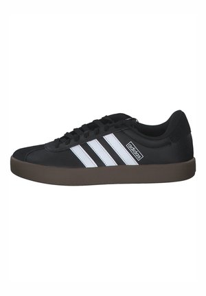 Baskets Adidas noires avec des bandes blanches, fermeture à lacets et semelle en caoutchouc marron, vue de côté.