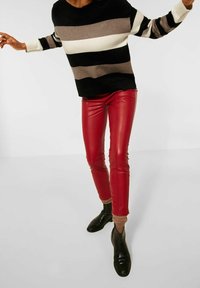 Randig svart och vit tröja med bruna detaljer, kombinerad med röda byxor i konstläder. Svarta ankelboots avlar hela outfiten.