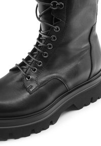 Stivale in pelle nera con lacci, caratterizzato da una suola robusta, punta arrotondata e occhielli in metallo. Il gambale è texturizzato con finiture lisce.