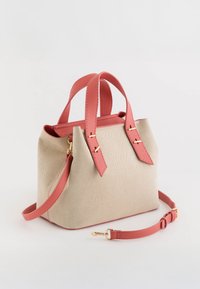 Beige canvas handtas met koraalkleurige leren handvatten, gouden hardware accenten en een gestructureerde vorm. Verstelbare schouderriem inbegrepen.
