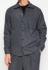 Šedá košile-jacket z vlněné směsi s límečkem, knoflíkovým zapínáním, jednou náprsní kapsou a dlouhými rukávy. Měkká textura s mírně boxy střihem.