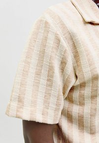 Chemise à manches courtes avec un motif rayé beige crémeux et pêche clair. Le tissu a une finition texturée et présente un col classique.
