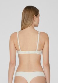Bralette beige con tirantes ajustables, un acabado suave y un cierre de gancho y ojal en la parte posterior; diseño simple y sin costuras.